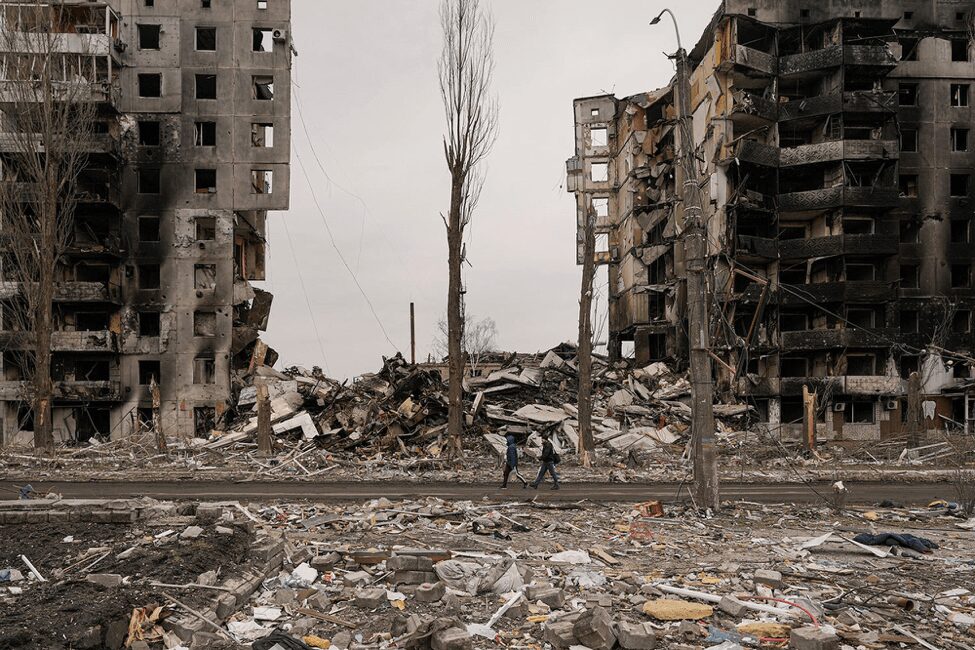 A view of two people in front of destroyed buildings and road