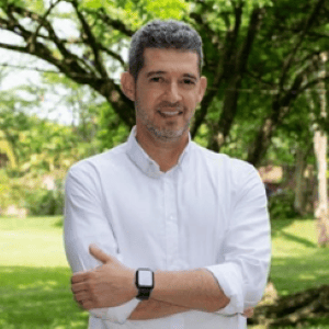 Man in white shirt standing outdoors with arms crossed, smiling.