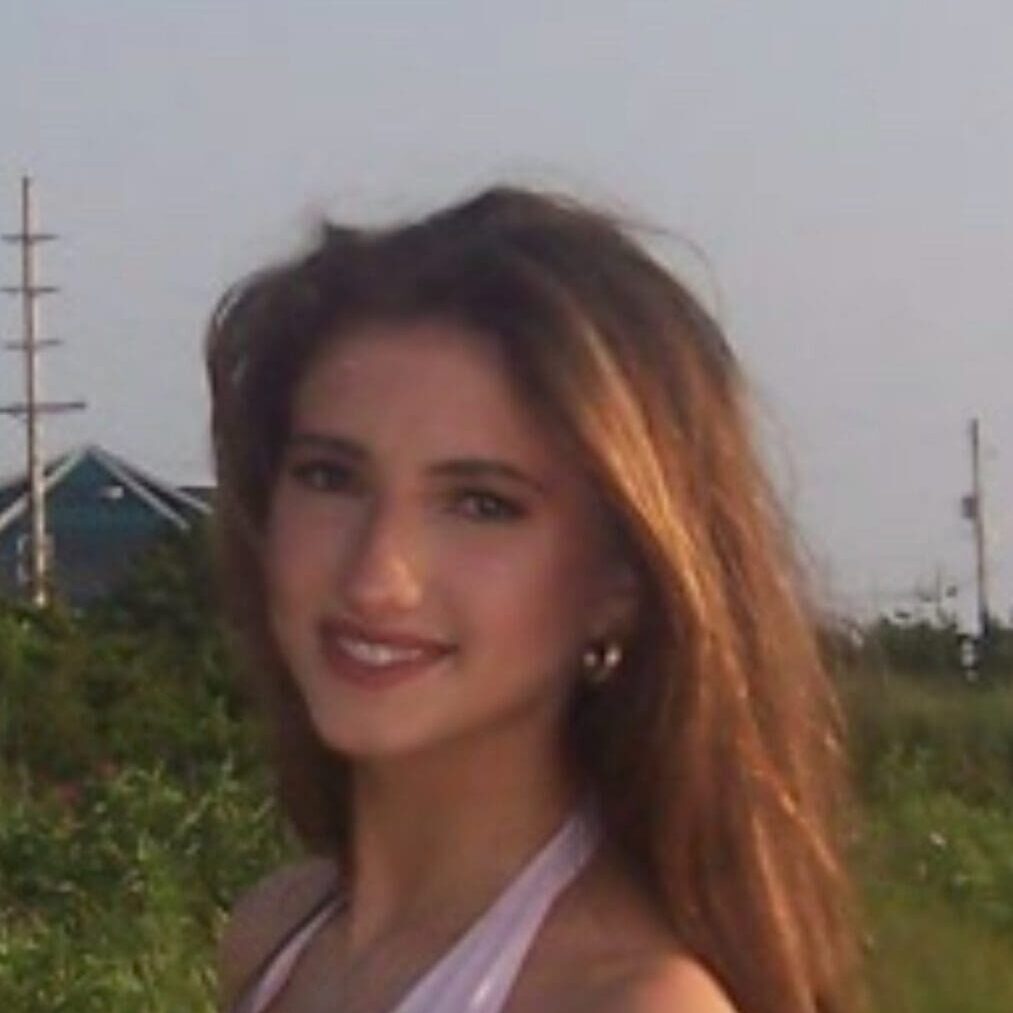 Young woman smiling outdoors with greenery and power lines behind.