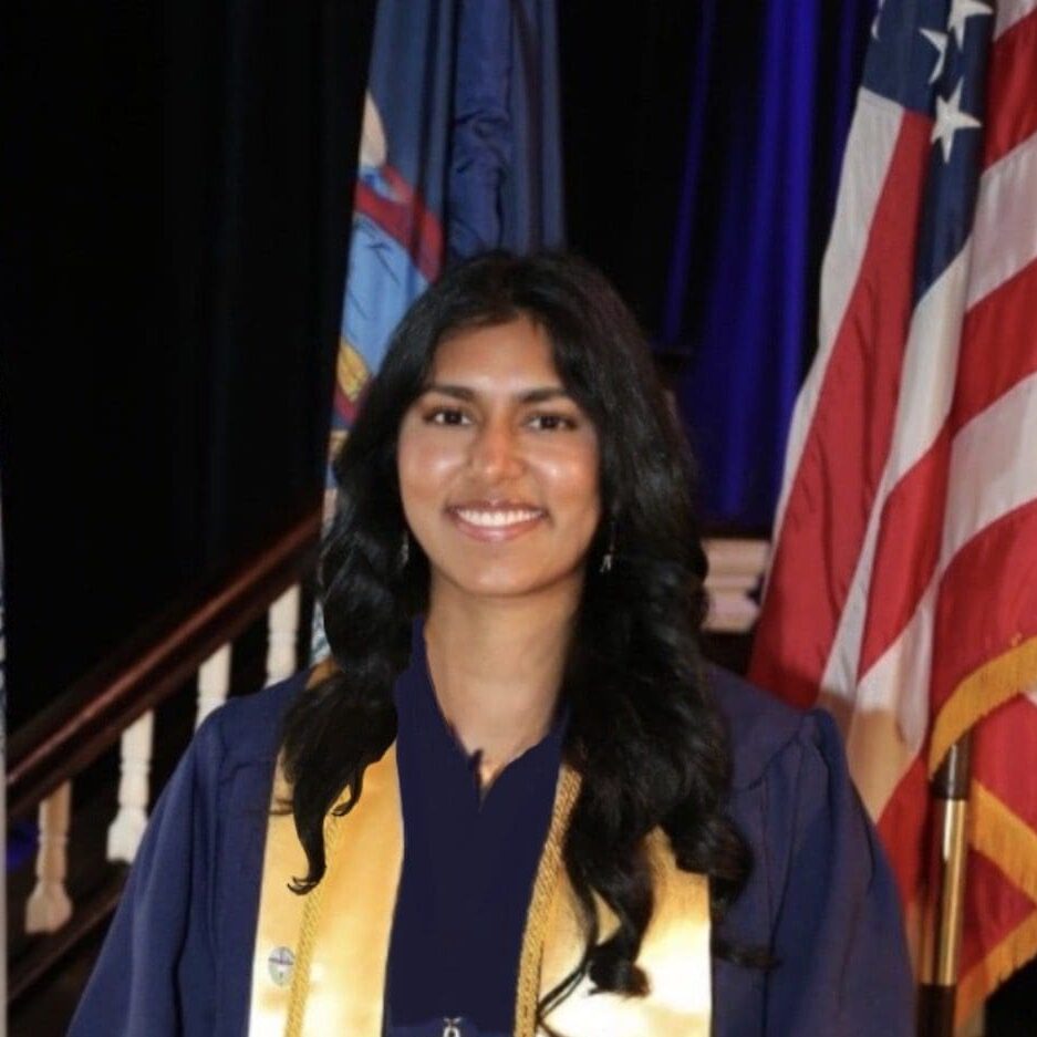 Graduate smiling in a cap and gown with American flag.