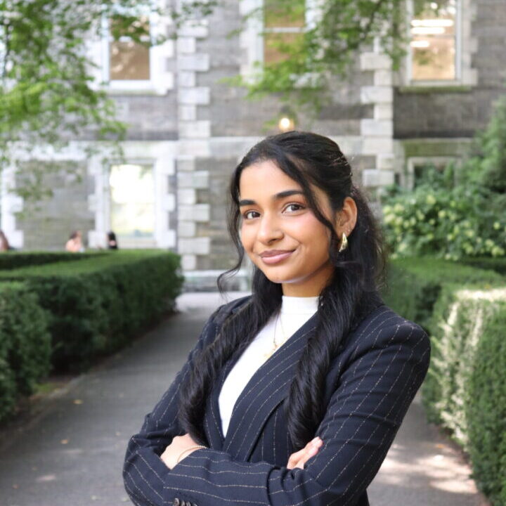Confident woman in a dark blazer stands outdoors with arms crossed.