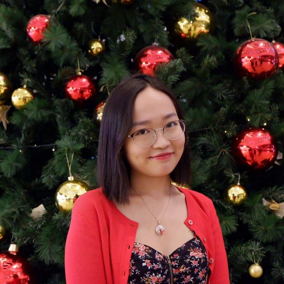 A woman smiling in front of a decorated Christmas tree.
