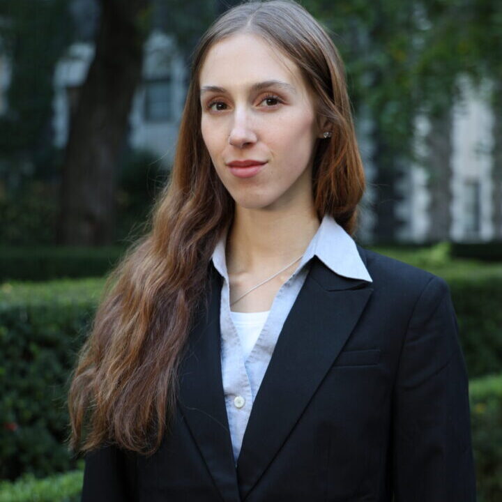 Professional young woman in a black suit posing outdoors.