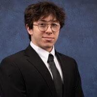 Young man in glasses and suit posing against a blue backdrop.