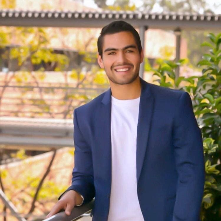 A smiling man in a blue blazer and white shirt outdoors.