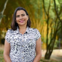 Smiling woman in a patterned blouse outdoors with blurred trees.