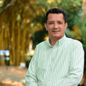Man in a green-striped shirt standing outdoors with trees in the background.
