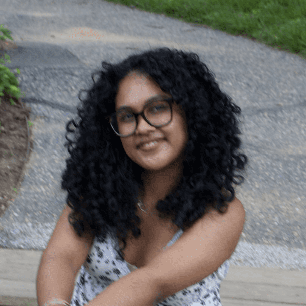 A smiling woman with curly hair and glasses sitting outdoors.