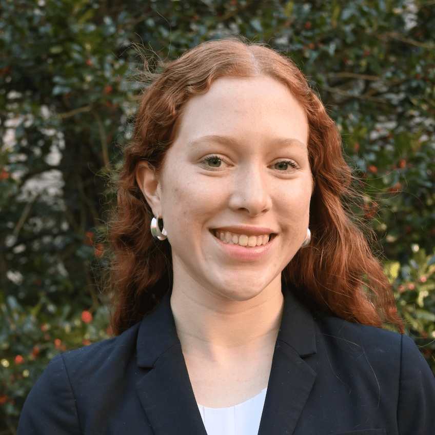 Smiling woman with red hair wearing a black blazer outdoors.