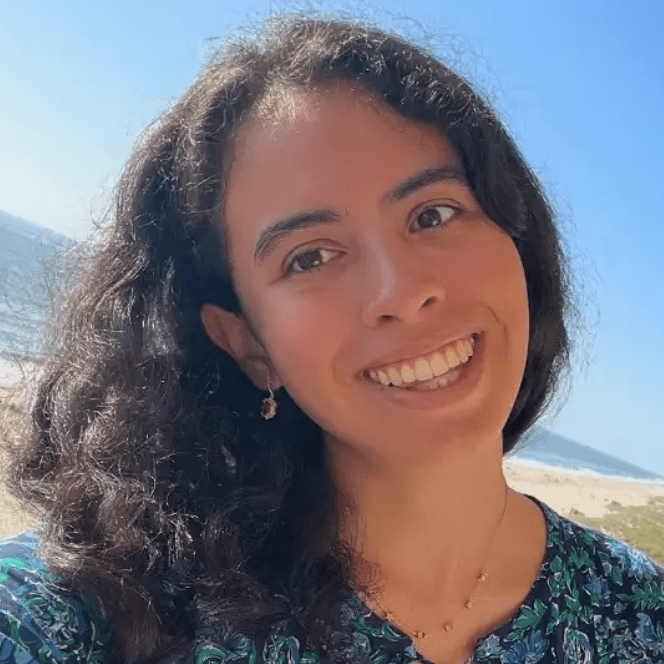 Smiling woman with curly hair posing outdoors on a sunny day.