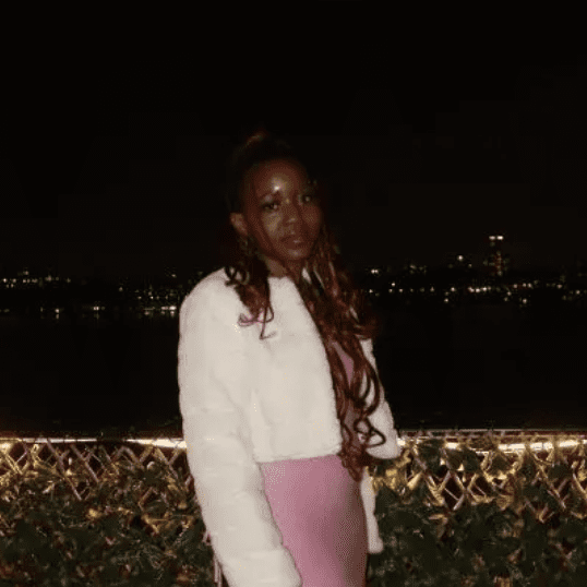 Woman posing outdoors at night with city lights in the background.
