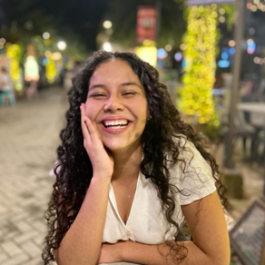 A joyful woman with curly hair smiling warmly outdoors at night.