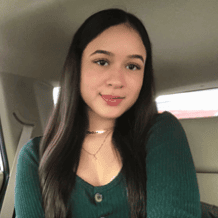 Young woman with long dark hair sitting in a car, smiling at the camera.
