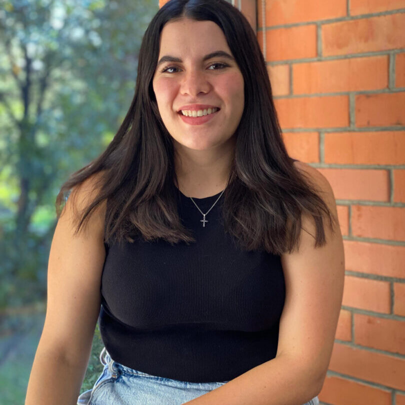 A young woman smiling outdoors against a brick wall.