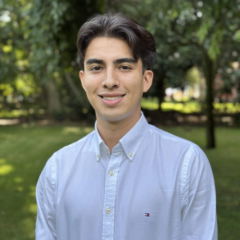 Young man in a white shirt smiling outdoors.