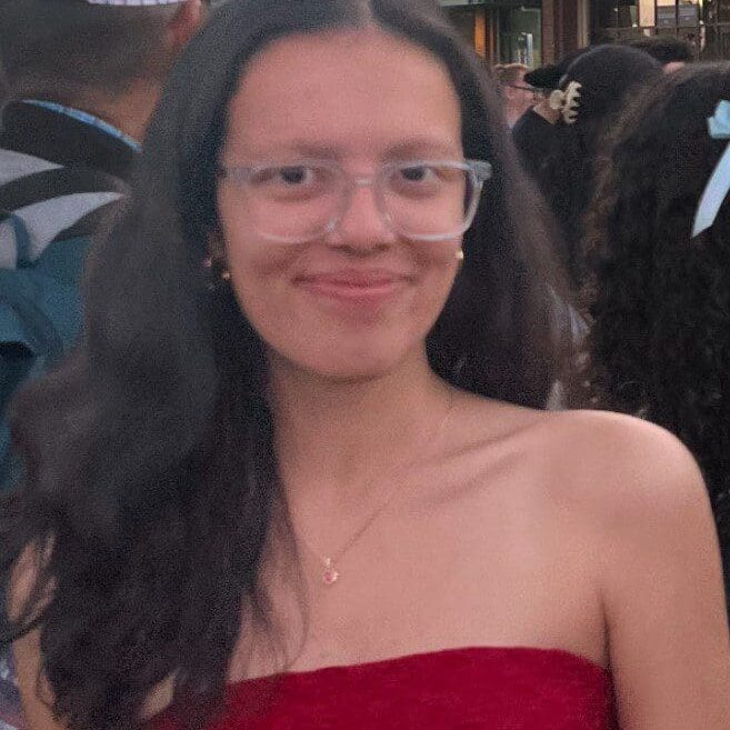 A smiling young woman with long dark hair and glasses wearing a red strapless top.