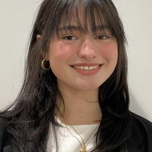 Smiling young woman with dark hair and gold hoop earrings.